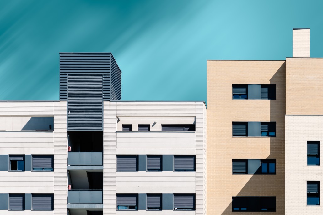 Contemporary apartment building facades with beige brick and white panels under a clear teal sky